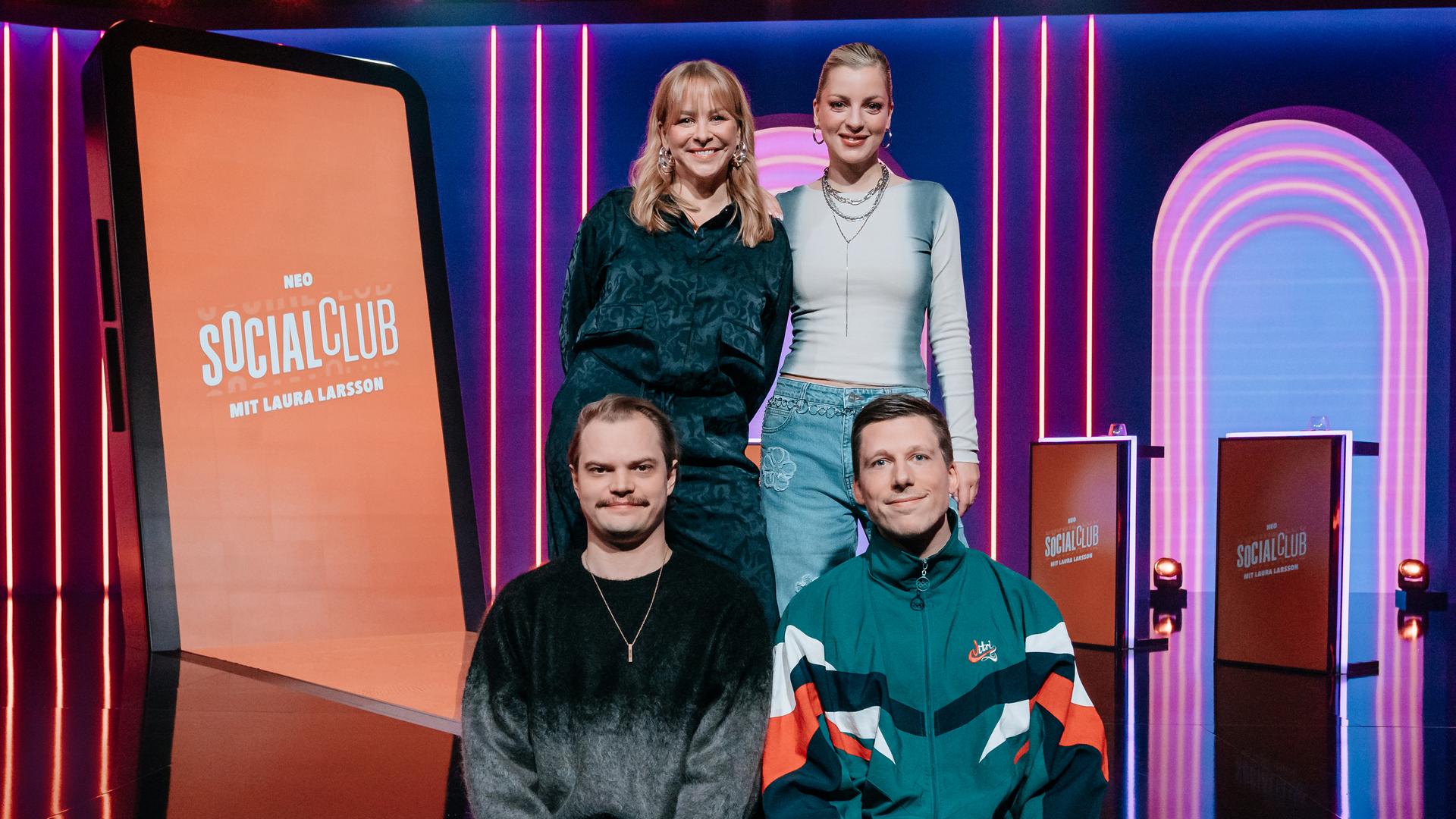 Auf der Streppe des Studios posieren Jasmin Schwiers (oben l.), Laura Larsson (oben r.), Wilson Gonzalez (unten l.) und Laura Larsson (unten r.) zusammen. Im Hintergrund steht ein überdimensionales Smartphone im Studio. 