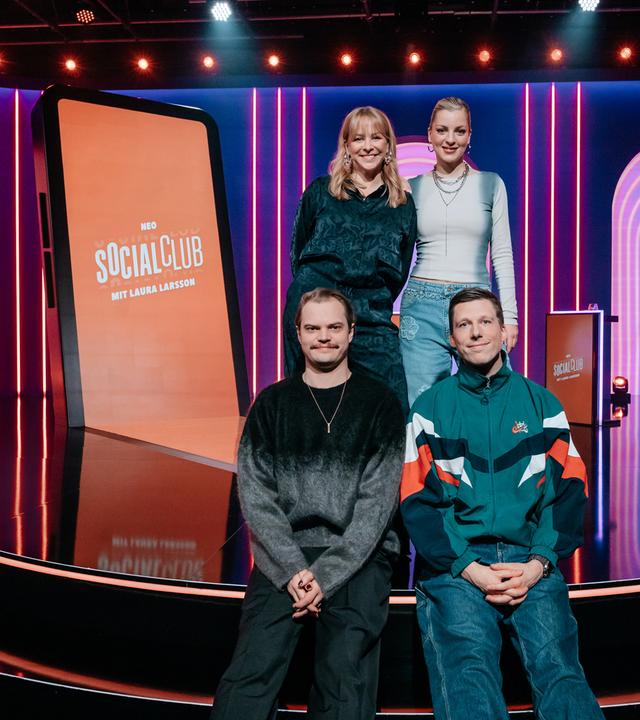 Auf der Streppe des Studios posieren Jasmin Schwiers (oben l.), Laura Larsson (oben r.), Wilson Gonzalez (unten l.) und Laura Larsson (unten r.) zusammen. Im Hintergrund steht ein überdimensionales Smartphone im Studio. 