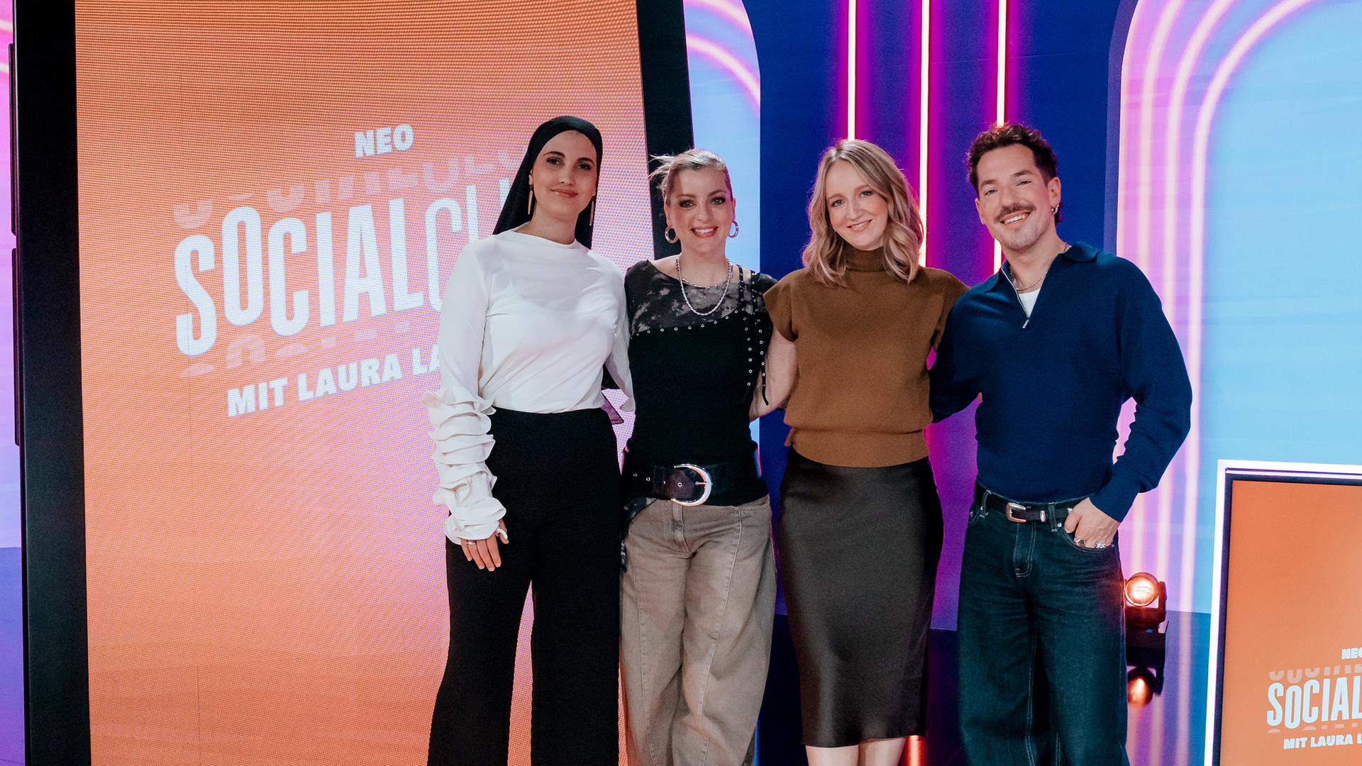 Anissa Loucif, Laura Larsson, Mirella Precek und Nico Stank (v.r.n.l.) posieren zusammen im Studio vor einem überdimensionalen Smartphone-Bildschirm.