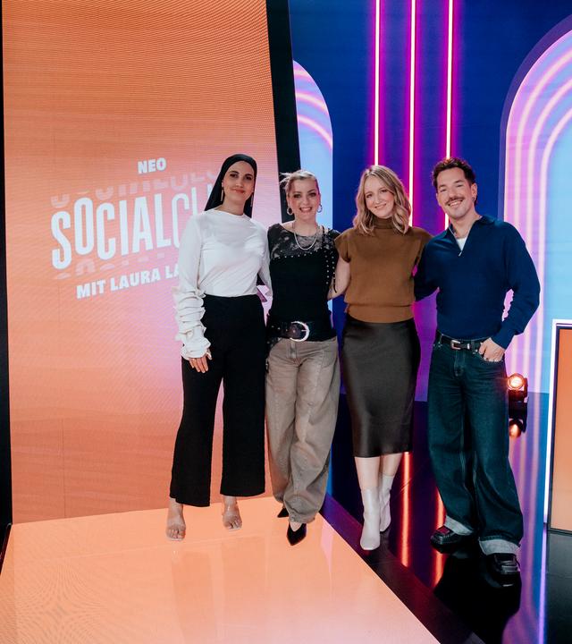 Anissa Loucif, Laura Larsson, Mirella Precek und Nico Stank (v.r.n.l.) posieren zusammen im Studio vor einem überdimensionalen Smartphone-Bildschirm.