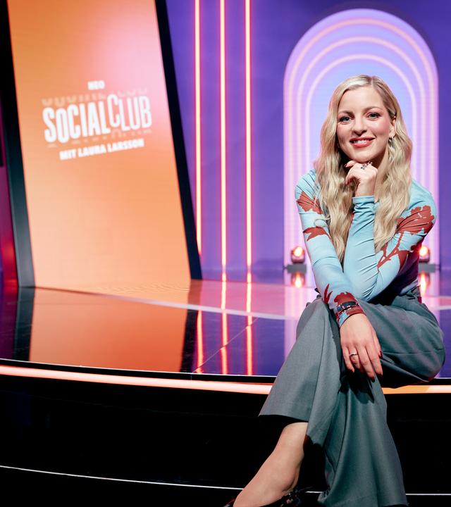 Laura Larsson sitzt auf einer Treppe im Studio des Formats "Neo Social Club" und schaut in die Kamera.