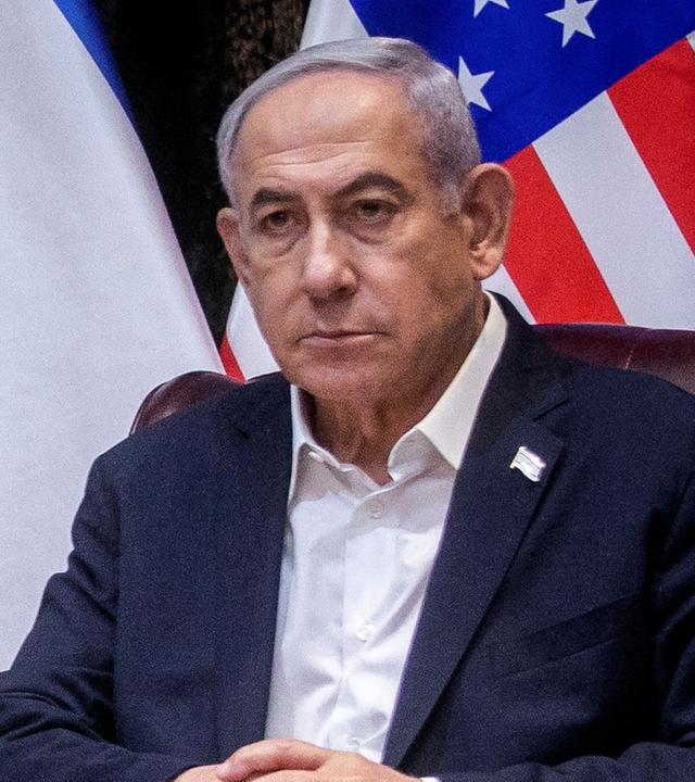 Benjamin Netanjahu, ein älterer Mann mit grauen Haaren, sitzt vor einer israelischen und einer US-amerikanischen Flagge in einer Pressekonferenz.