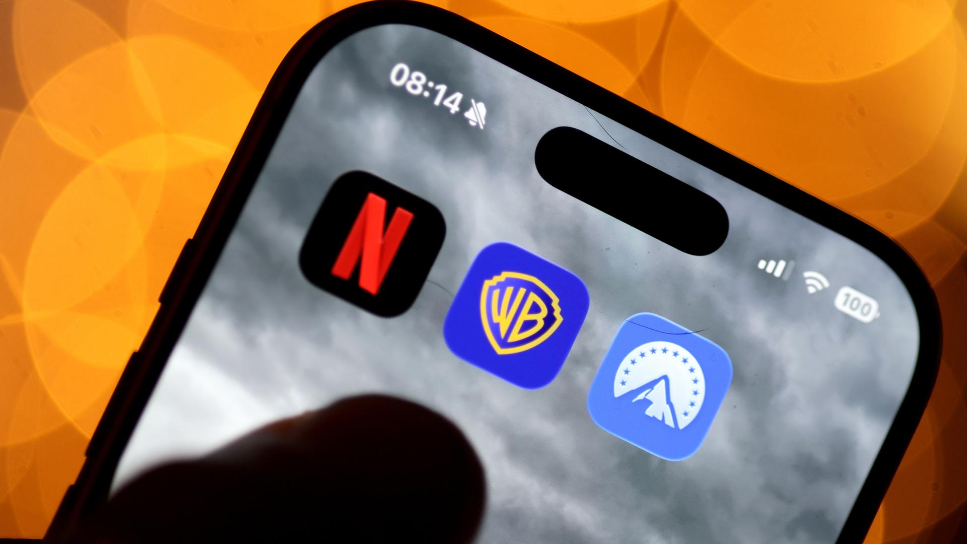 Auf einem Handy sind die Apps von Netflix, Paramount und Warner Bros. nebeneinander zu sehen.