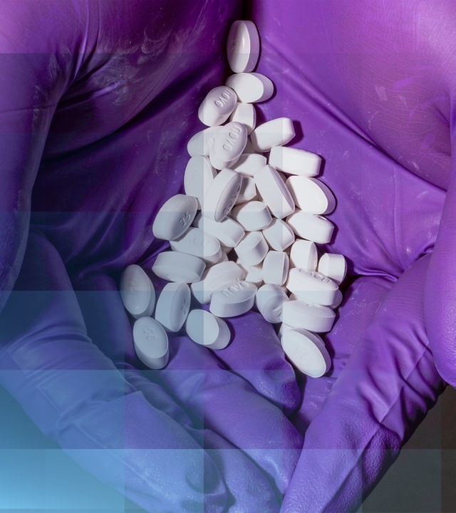 In einer mit Handschuhen bedeckten Hand liegen zahlreiche Tabletten