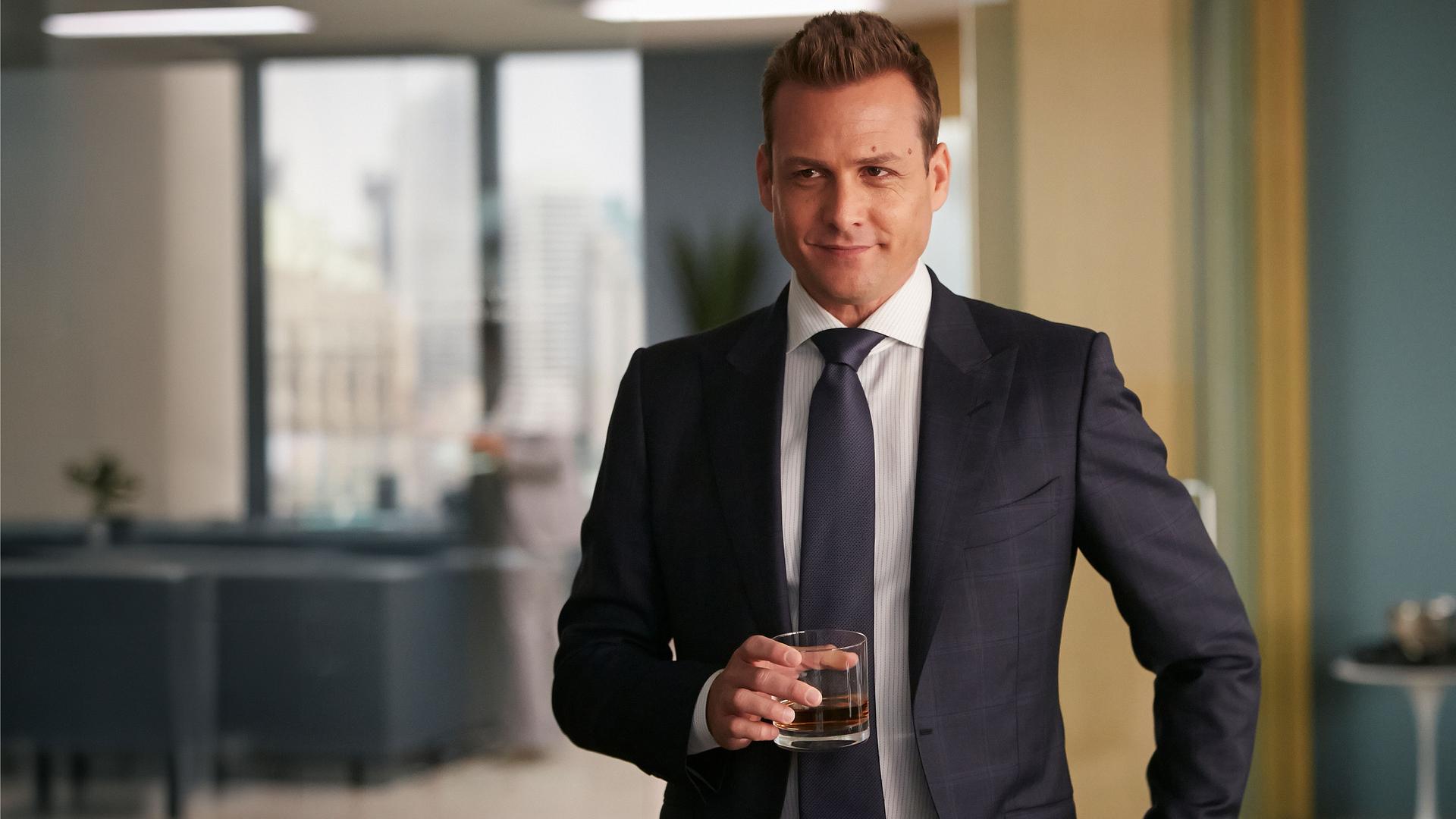 "Suits - Neue Ufer": Harvey (Gabriel Macht) steht in seinem Büro und hält elegant gekleidet mit einem siegesgewissen Gesichtsausdruck ein Whiskeyglas in der Hand.