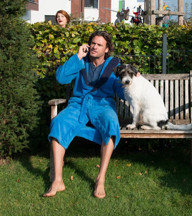Jan (Stephan Luca) sitzt telefonierend mit seinem Hund auf einer Bank im Garten. Im Nachbargarten hängt Kerstin Matzerath (Susanne Böwe) lauschend ihre Dessous an eine Wäscheleine.
