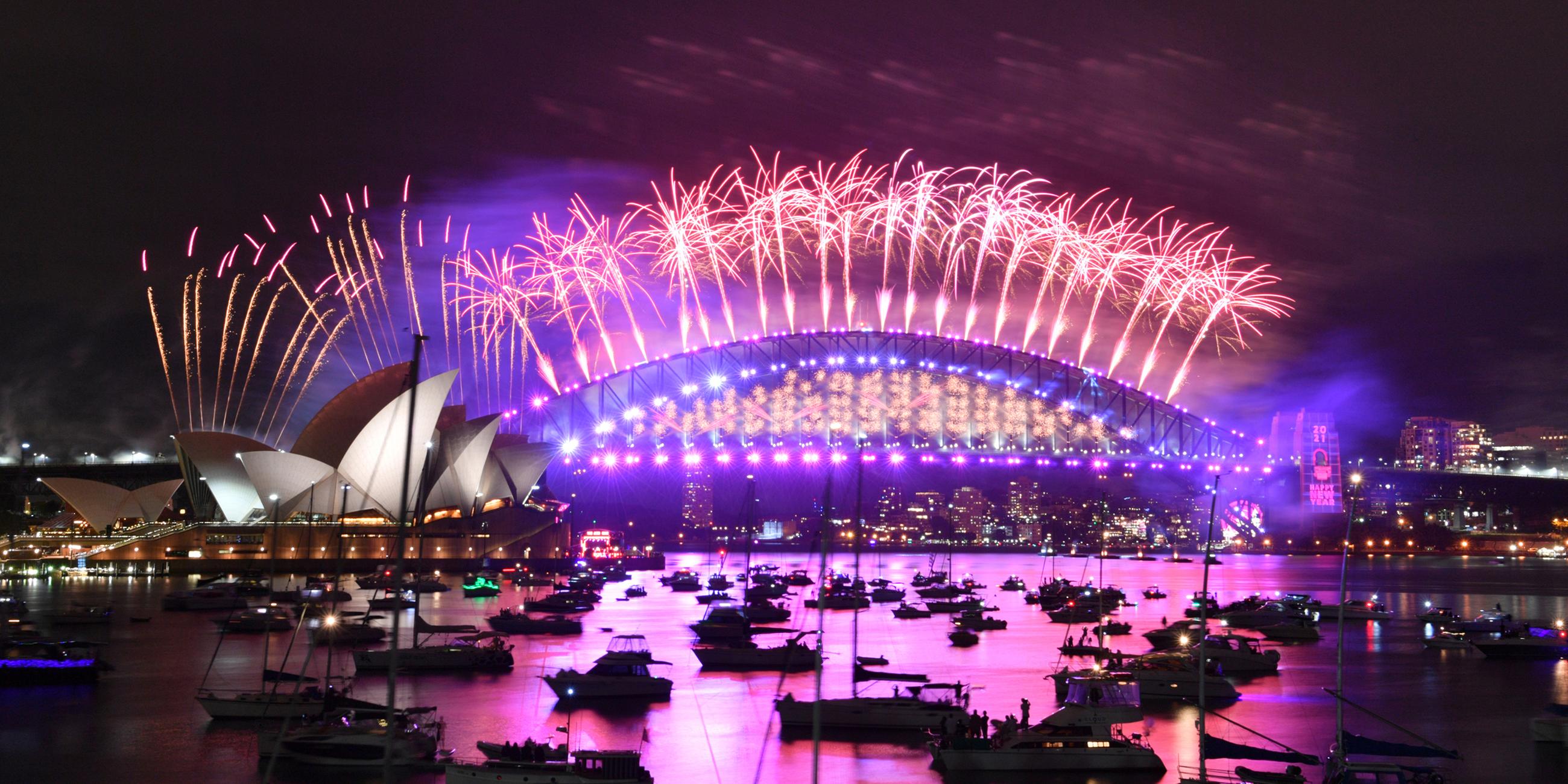 Im Hafen von Sydney treibende Boote werden vom Feuerwerk beleuchtet, das von der Harbour Bridge und dem Opernhaus (l) aus gestartet wird.