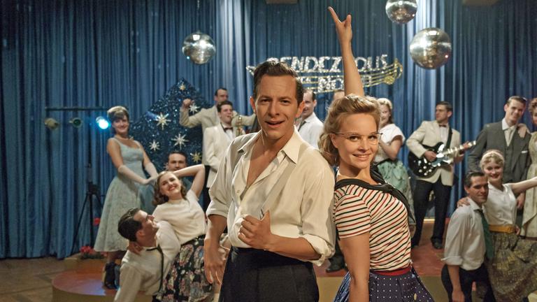 "Ku'damm 59": Monika Schöllack (Sonja Gerhardt, m.r.) und Freddy Donath (Trystan Pütter, m.l.) stehen im Vordergrund und posieren für die Kamera. Im Hintergrund posieren weitere Darsteller der Fernsehshow "Rendezvous nach Noten".