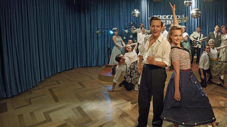 "Ku'damm 59": Monika Schöllack (Sonja Gerhardt, m.r.) und Freddy Donath (Trystan Pütter, m.l.) stehen im Vordergrund und posieren für die Kamera. Im Hintergrund posieren weitere Darsteller der Fernsehshow "Rendezvous nach Noten".