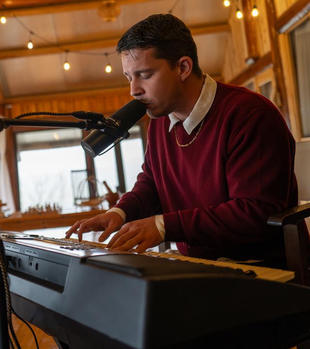 Nico Santos sitzt und spielt auf einem Keyboard und singt dabei in ein Mikrofon, das vor ihm steht. 