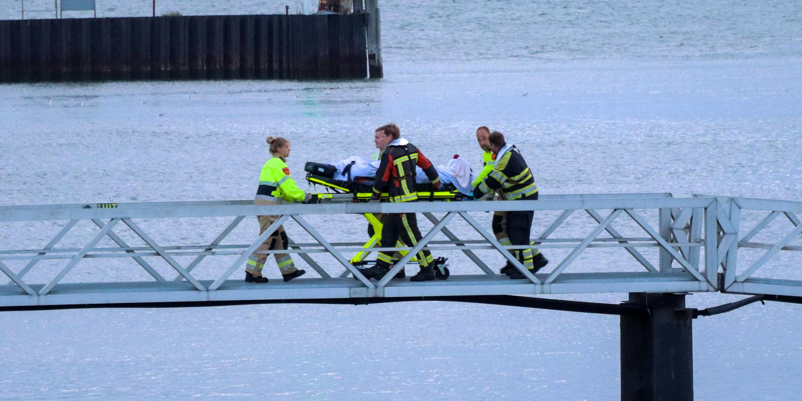 Einsatzkräfte bringen einen Verletzten über eine Brücke in einem Hafen.