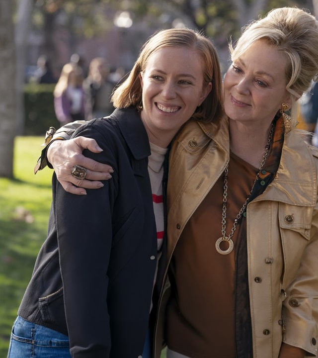"Hacks - Niemals für einen Witz entschuldigen": Deborah (Jean Smart) lächelt und umarmt Ava Hannah Einbinder), die ebenso gelöst und glücklich lacht. Im Hintergrund befinden sich, unscharf zu erkennen, weitere Personen (Komparsen) unter Bäumen.