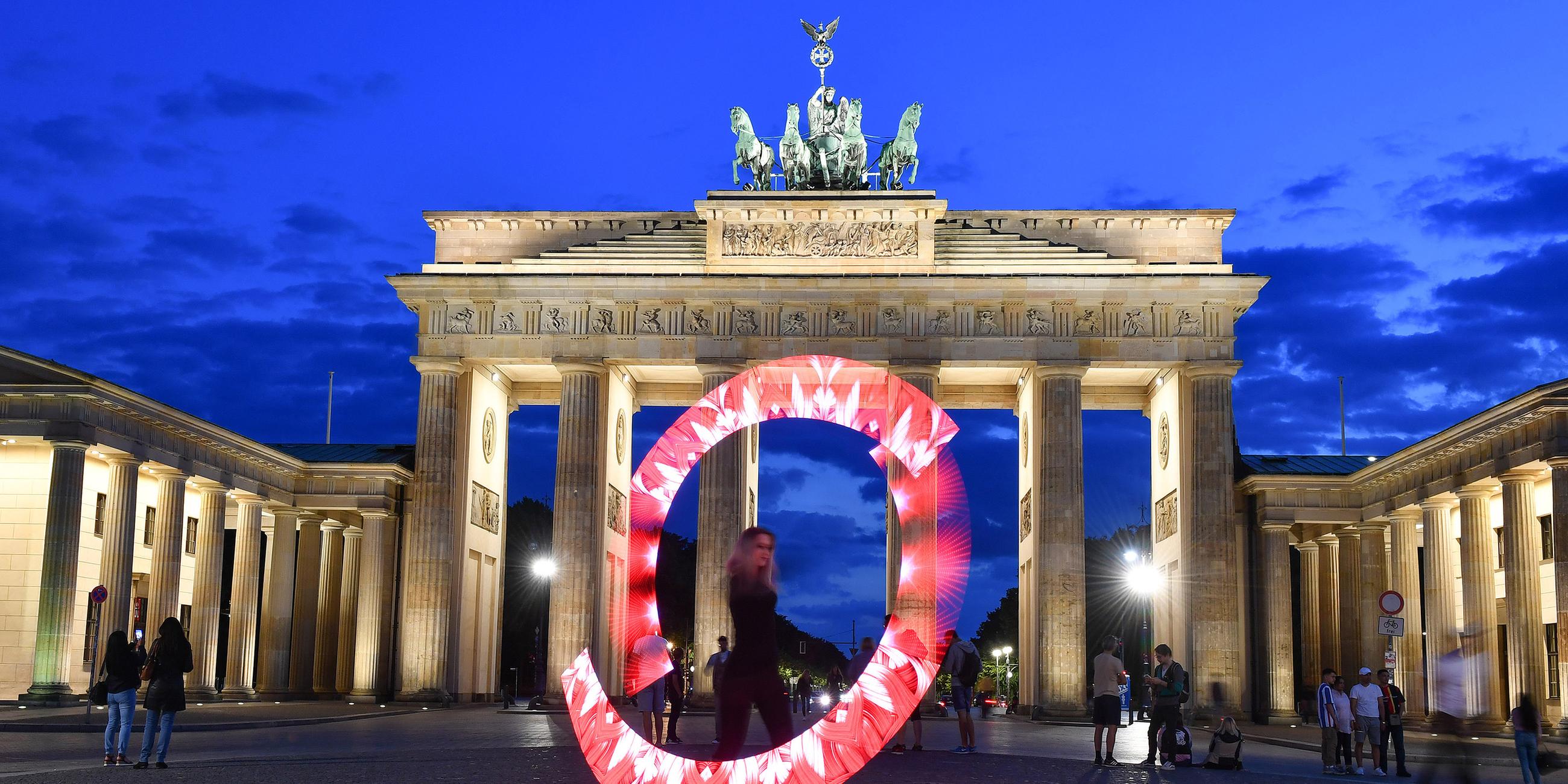 Eine Lichtkünstlerin zaubert mit roten Lichtern einen Leuchtkranz vor das Brandenburger Tor.