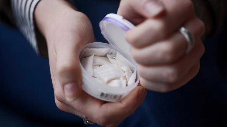 Eine Frau öffnet eine Dose mit tabakfreiem weißen Snus.