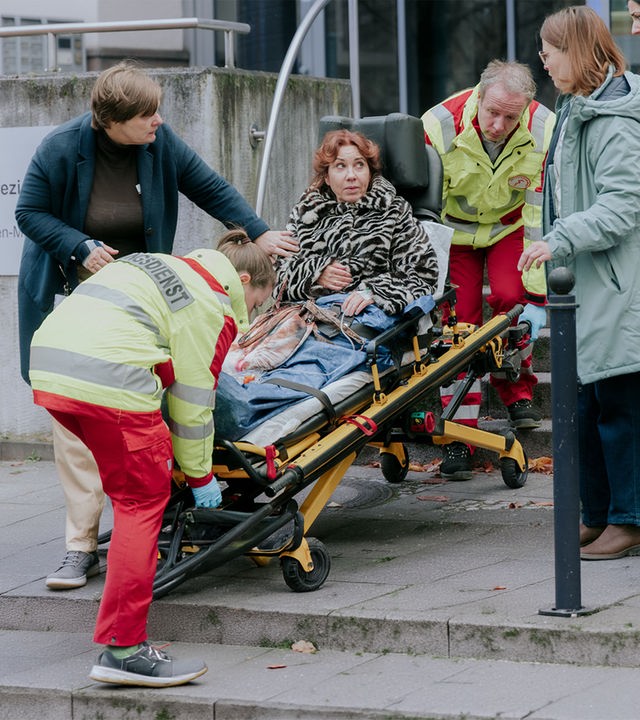 "Nine to Five - Das Amt - ABC Alarm": Doris (Kathrin Angerer) wird auf einer Trage von zwei Sanitätern (Komparsen) abtransportiert. Gisela (Petra Hartung), Conny (Lisa Hrdina), Dilara (Roxana Samadi) und Melissa (Anna Herrmann) haben sich um Doris versammelt.