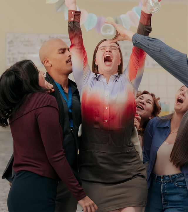 "Nine to Five - Das Amt - Connys Geburtstag": Dilara (Roxana Samadi), Can (Charles Booz Jakob), Doris (Kathrin Angerer) und Melissa (Anna Herrmann) haben sich um Conny (Lisa Hrdina) versammelt, blicken zu ihr und halten eine Flasche über sie. Conny hat die Hände nach oben gerissen und die Augen geschlossen.