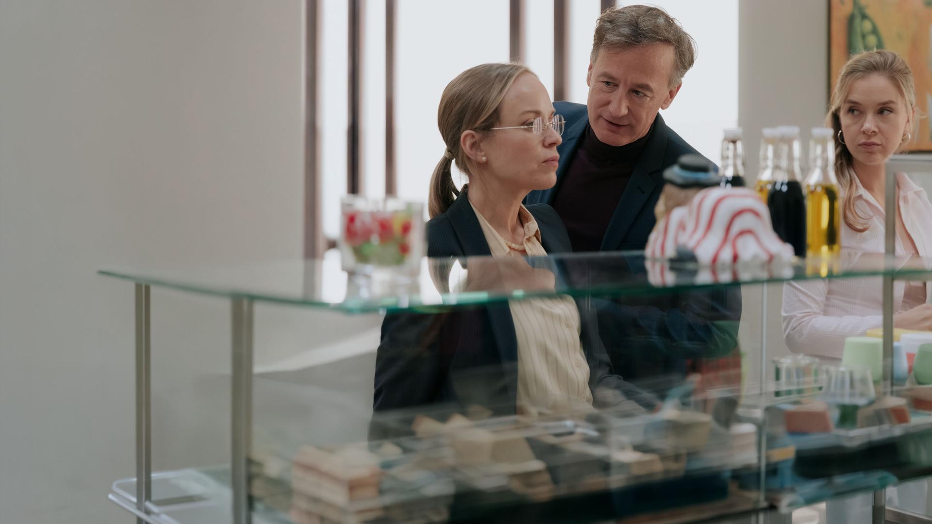 "Nine to Five - Das Amt - Tag 1": Ronja Keller (Friederike Kempter), Amtsleiter Schulenberg (Jan Henrik Stahlberg) und Melissa Seibel (Anna Herrmann) stehen nebeneinander vor der Theke in der Kantine. Georg blickt zu Ronja, Ronja blickt in die Ferne. Melissa beobachtet die beiden.