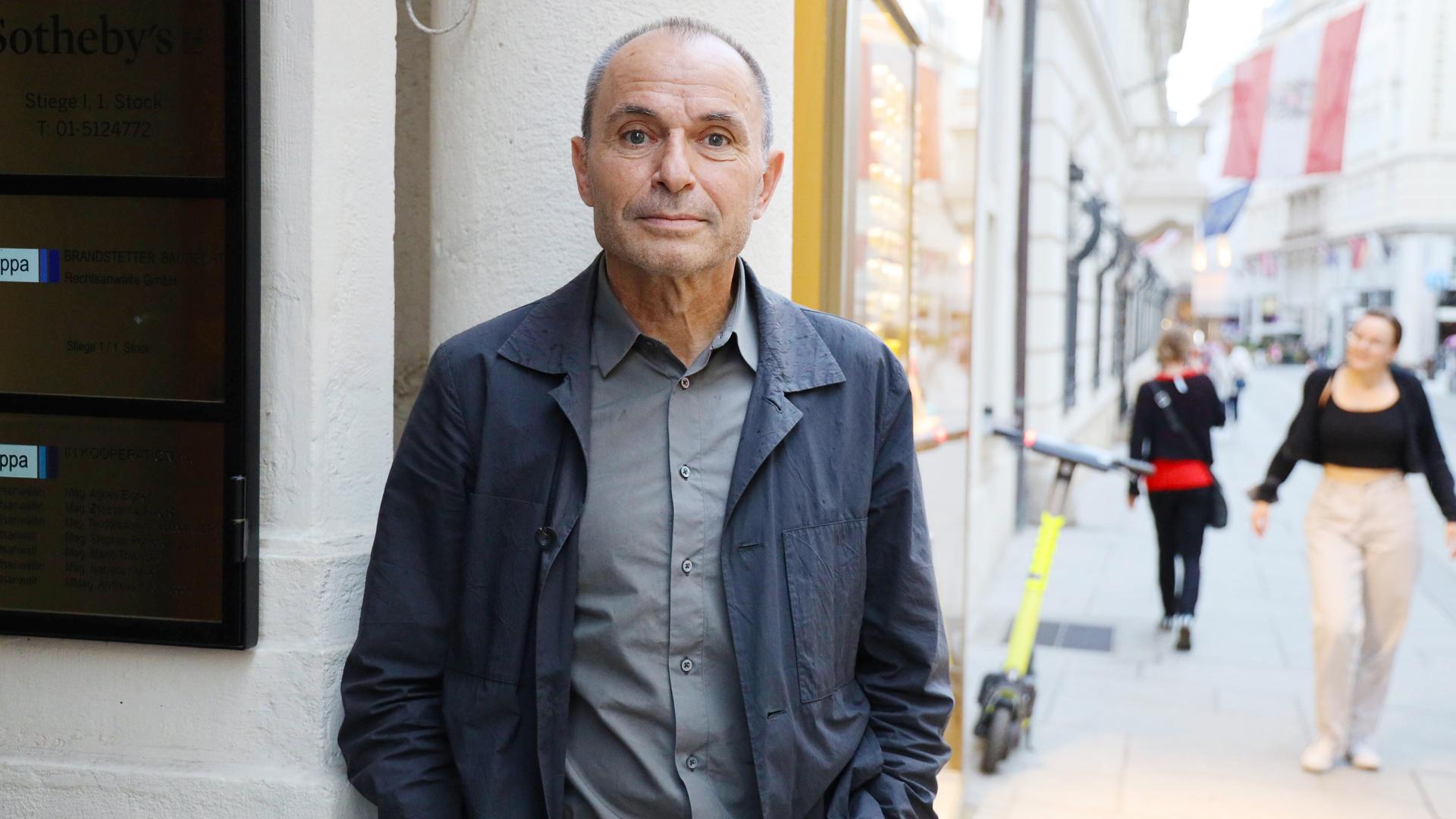 Ein älterer Mann imd unkelgrauen Anzug steht an einer Straßenecke.