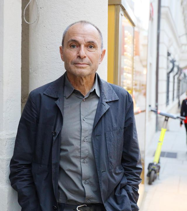 Ein älterer Mann imd unkelgrauen Anzug steht an einer Straßenecke.