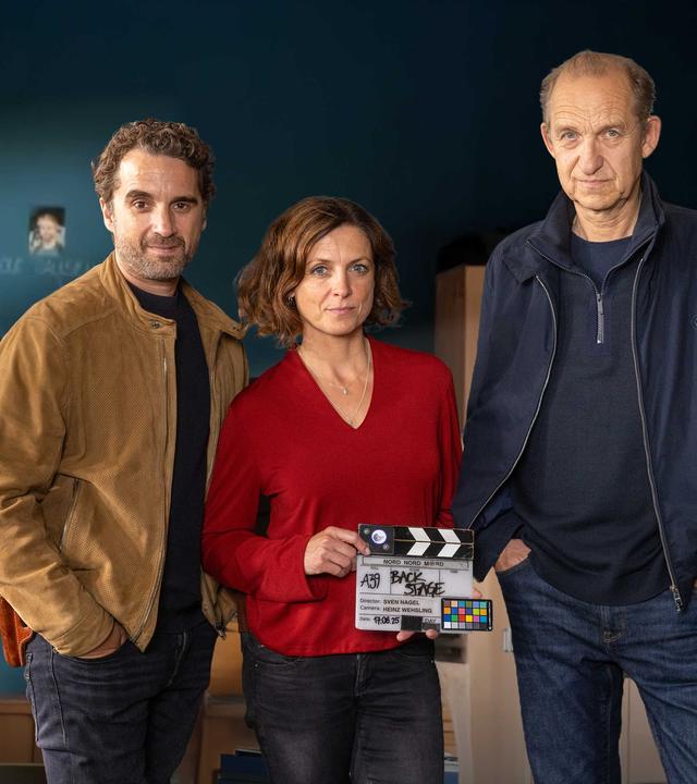 Oliver Wnuk, Julia Brendler und Peter Heinrich Brix vor der berühmten Tafel von Nord Nord Mord