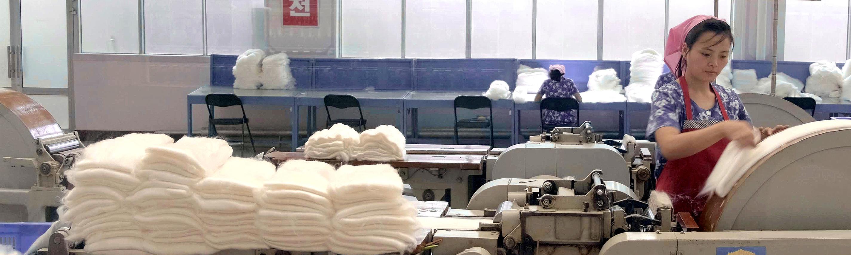 Textilarbeiterin mit Kopftuch an einer Maschine.