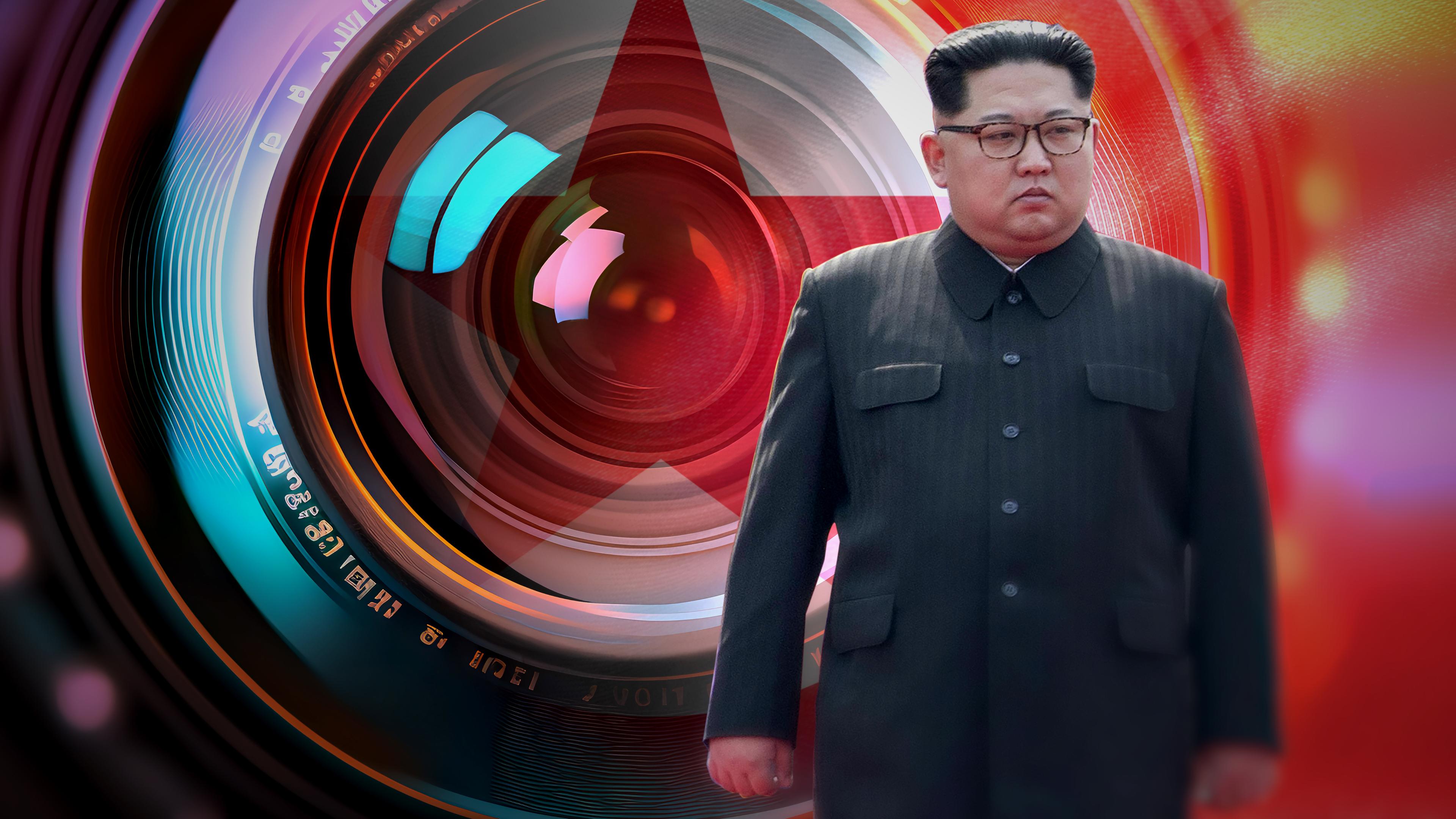 Kim Jong-un vor einer riesigen Kameralinse, dahinter angedeutet die Nordkoreanische Flagge.
