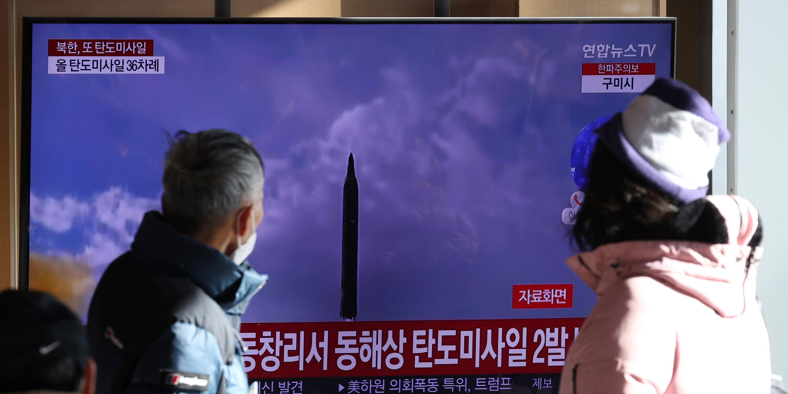 Südkorea, Seoul: Menschen sehen auf einen Fernsehbildschirm, auf dem eine Nachrichtensendung über den nordkoreanischen Raketenstart mit Filmmaterial gezeigt wird, im Bahnhof von Seoul.