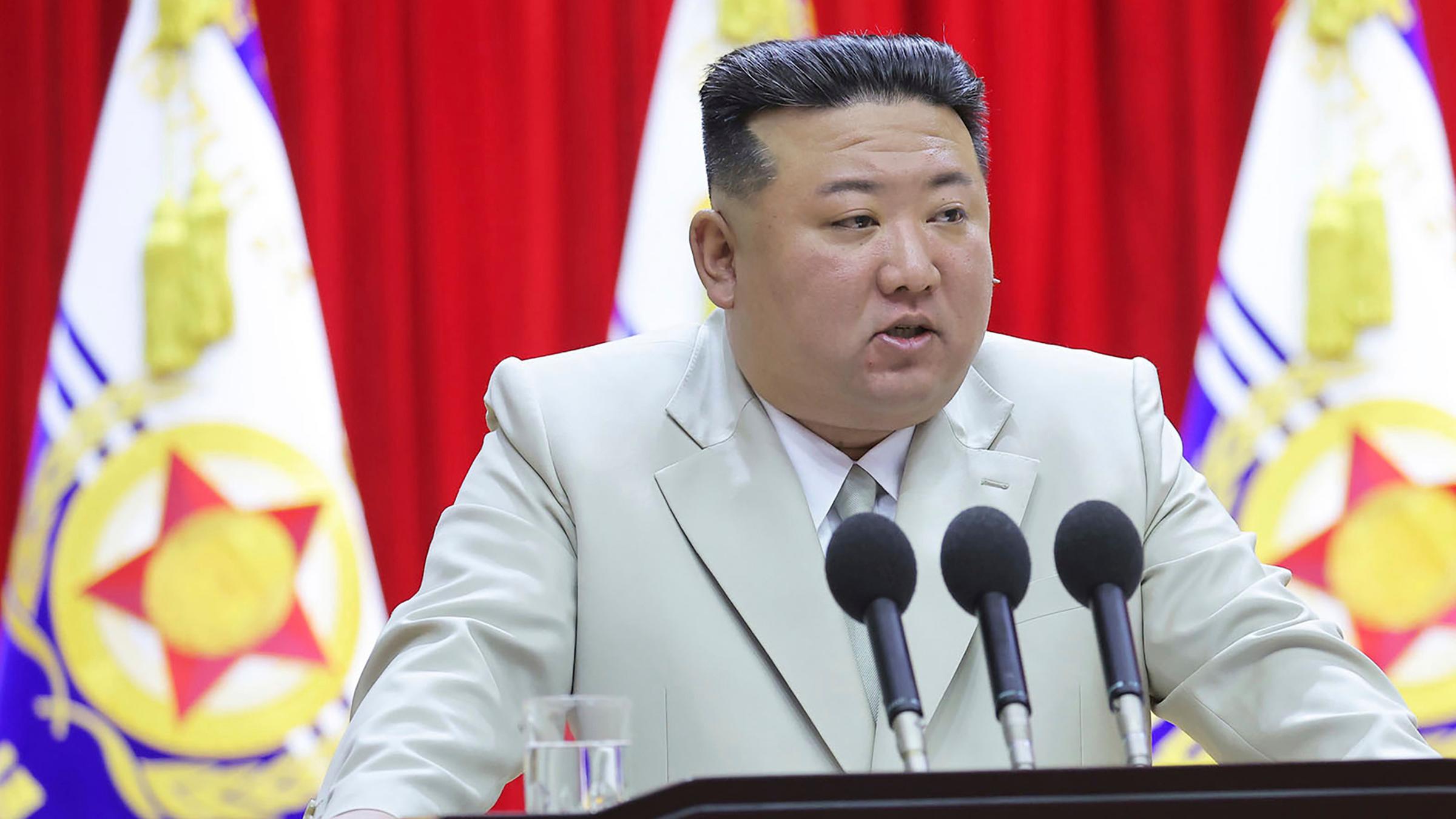 Kim Jong-un steht vor drei Mikrofonen im hellen Anzug.