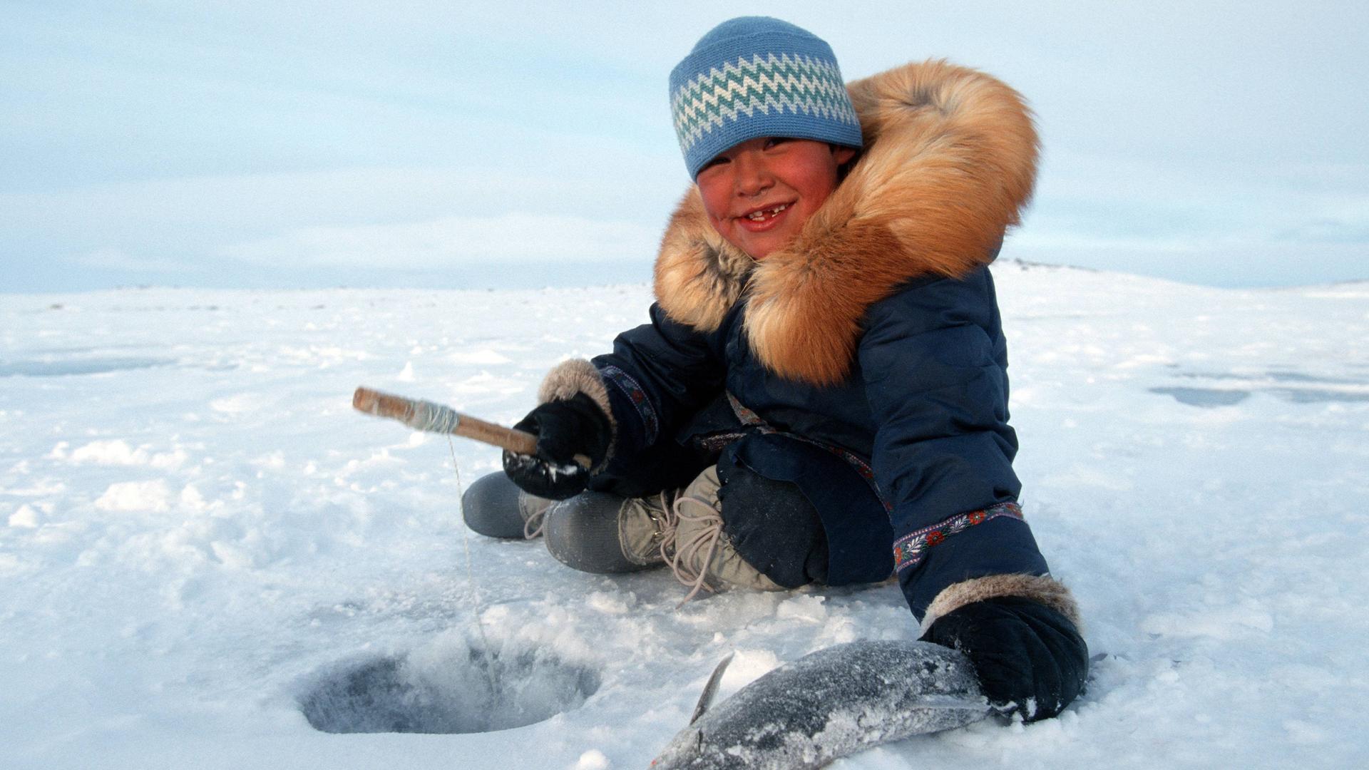 Inuit Junge stolz mit seinem gefangenen Fisch beim Eisangeln