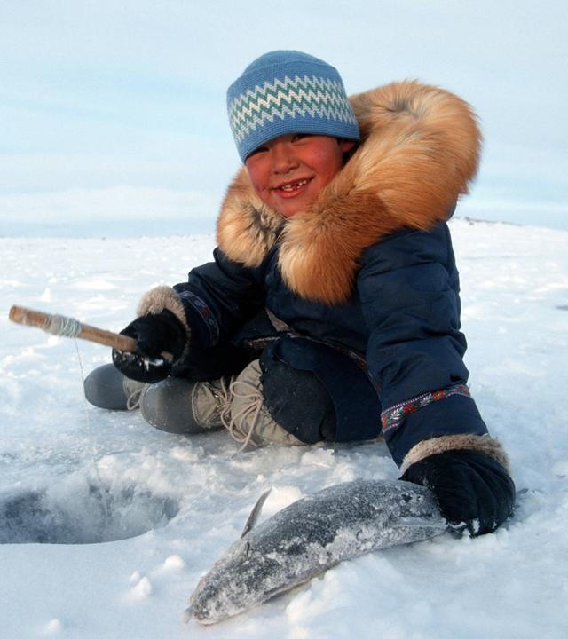 Inuit Junge stolz mit seinem gefangenen Fisch beim Eisangeln
