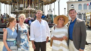 Hochzeitsplaner Tom (Jan Hartmann), Wally (Diana Körner), Kai (Moritz von Zeddelmann), Charlotte (Teresa Klamert) und Franziska (Annika Schrumpf) stehen vor einem Karussell nebeneinander und lächeln.