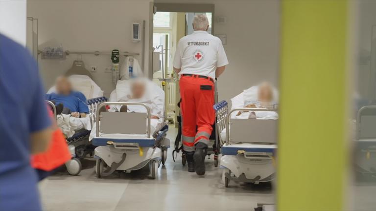 Zu sehen ist ein Raum in dem mehrere menschen in Krankenbetten liegen 