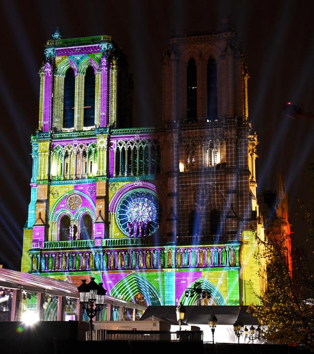 Die Kathedrale Notre Dame de Paris wird bei Nacht mit bunten Lichtern angestrahl.