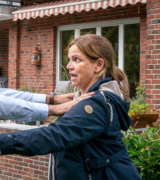 Barbara Weigand (Rebecca Immanuel) und Sascha Riss (Beat Marti) stehen auf einem Rasen im Garten eines roten Backsteinhauses gegenüber. Sascha wehrt Barbara mit beiden Händen ab, die nach ihm greift. Beide sehen sich wütend an.