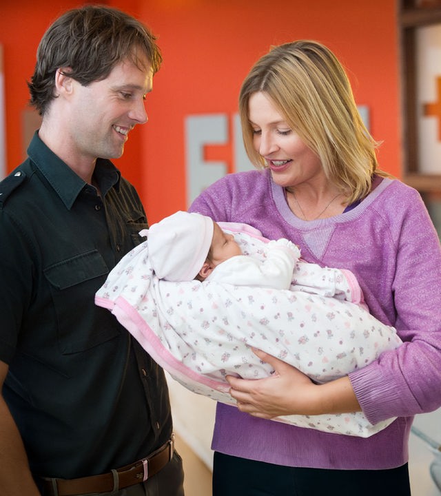 "Notruf Hafenkante - Ein neues Leben": Melanie (Sanna Englund) hält ein Baby im Arm, das sie und Mattes (Matthias Schloo), der neben ihr steht, lächelnd betrachten.