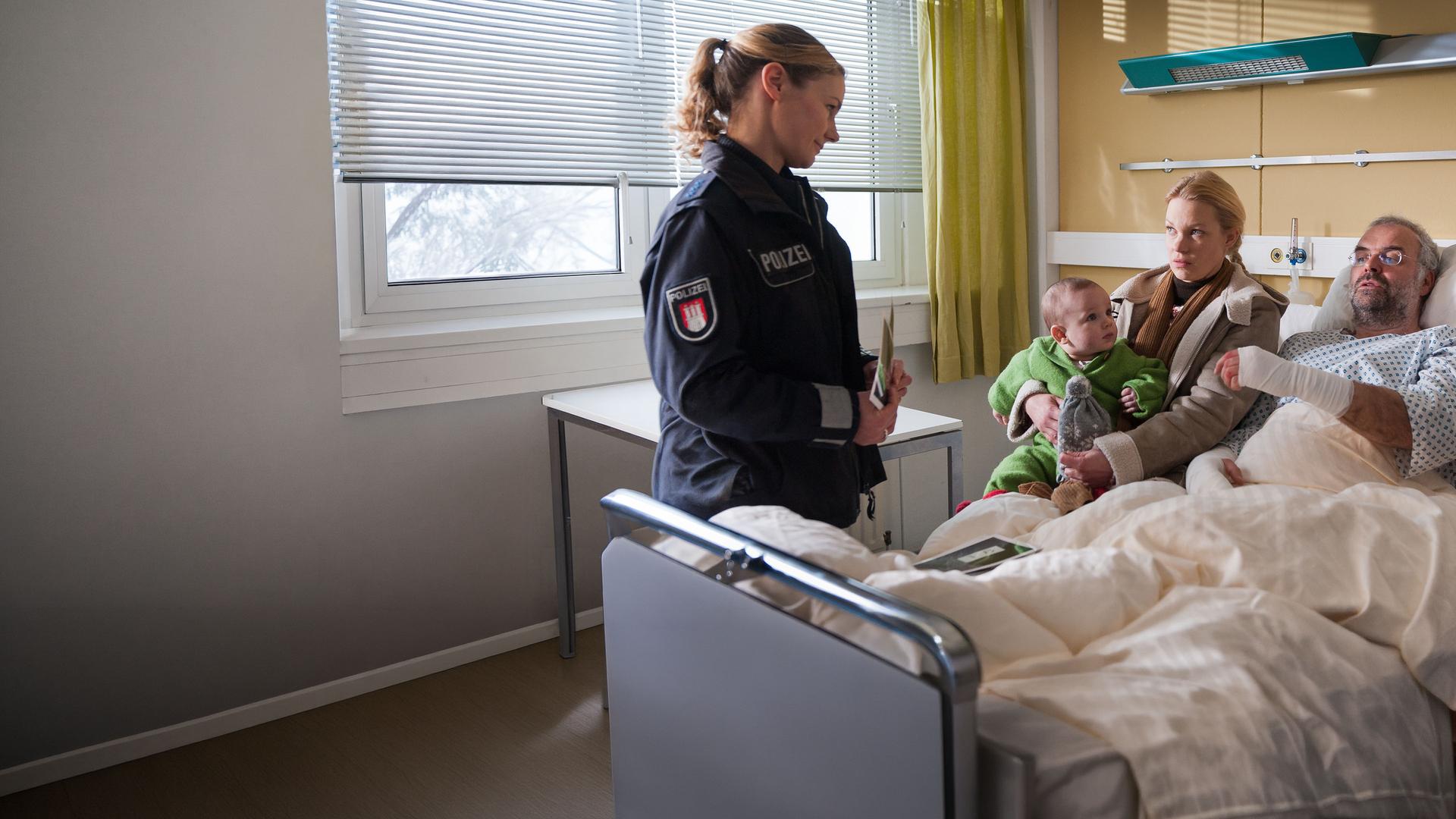 "Notruf Hafenkante - Leben daneben": Franzi (Rhea Harder) befragt Annik Karberg (Theresa Hübchen) und ihren Freund Enno Rüfken (Jophi Ries), der im Krankenbett liegt. Annik hat ein Kleinkind auf dem Schoß.