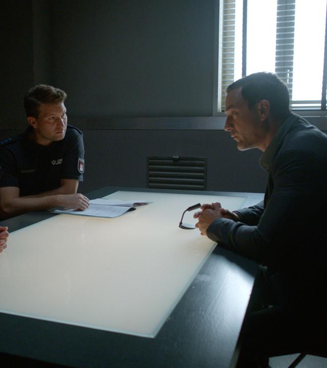 Die Polizistin Franzi Jung (Rhea Harder-Vennewald) und ihr Kollege Nick Brandt (Raúl Richter) sitzen nebeneinander an einem Tisch. Ihnen gegenüber sitzt Peter Schwartz (Sönke Möhring). Franzi und Nick sehen Schwartz an, er blickt zu Franzi.