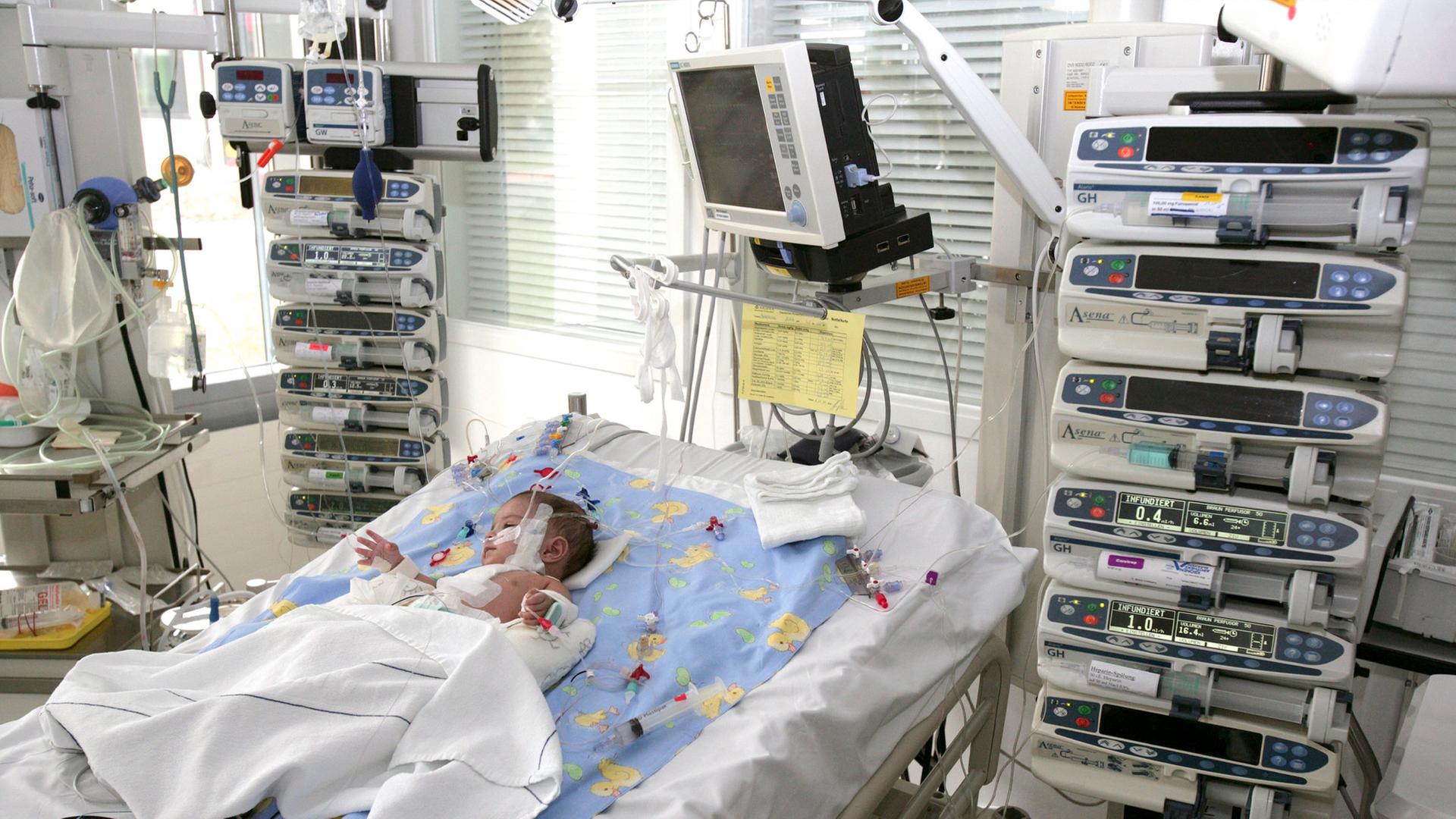 Ein Baby liegt in einem Krankenhausbett auf einer Intensivstation. Um das Bett sind medizinische Geräte aufgebaut.
