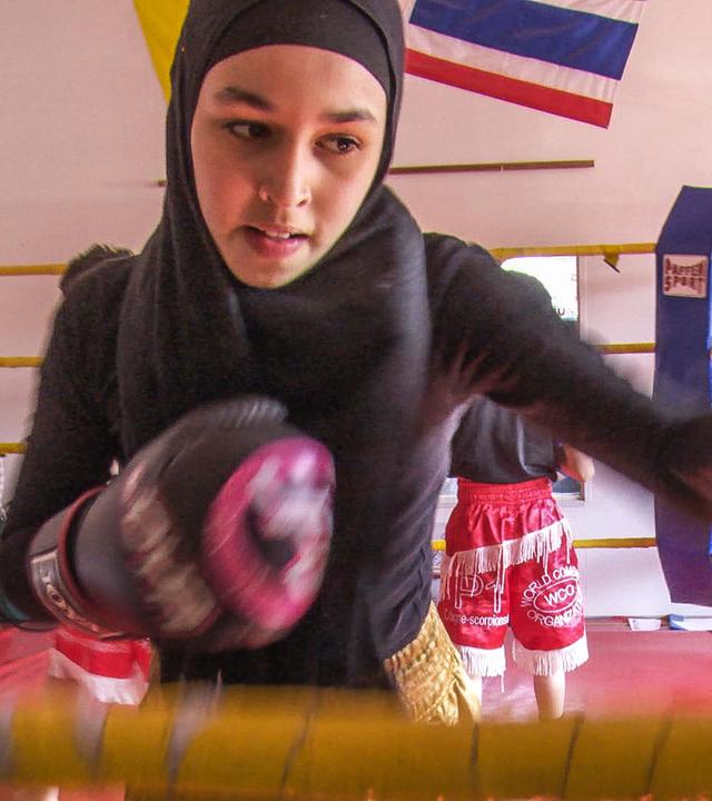 Nouhaila ist beim Training im Boxring. Sie trägt Boxhandschuhe und boxt gegen einen Boxsack.