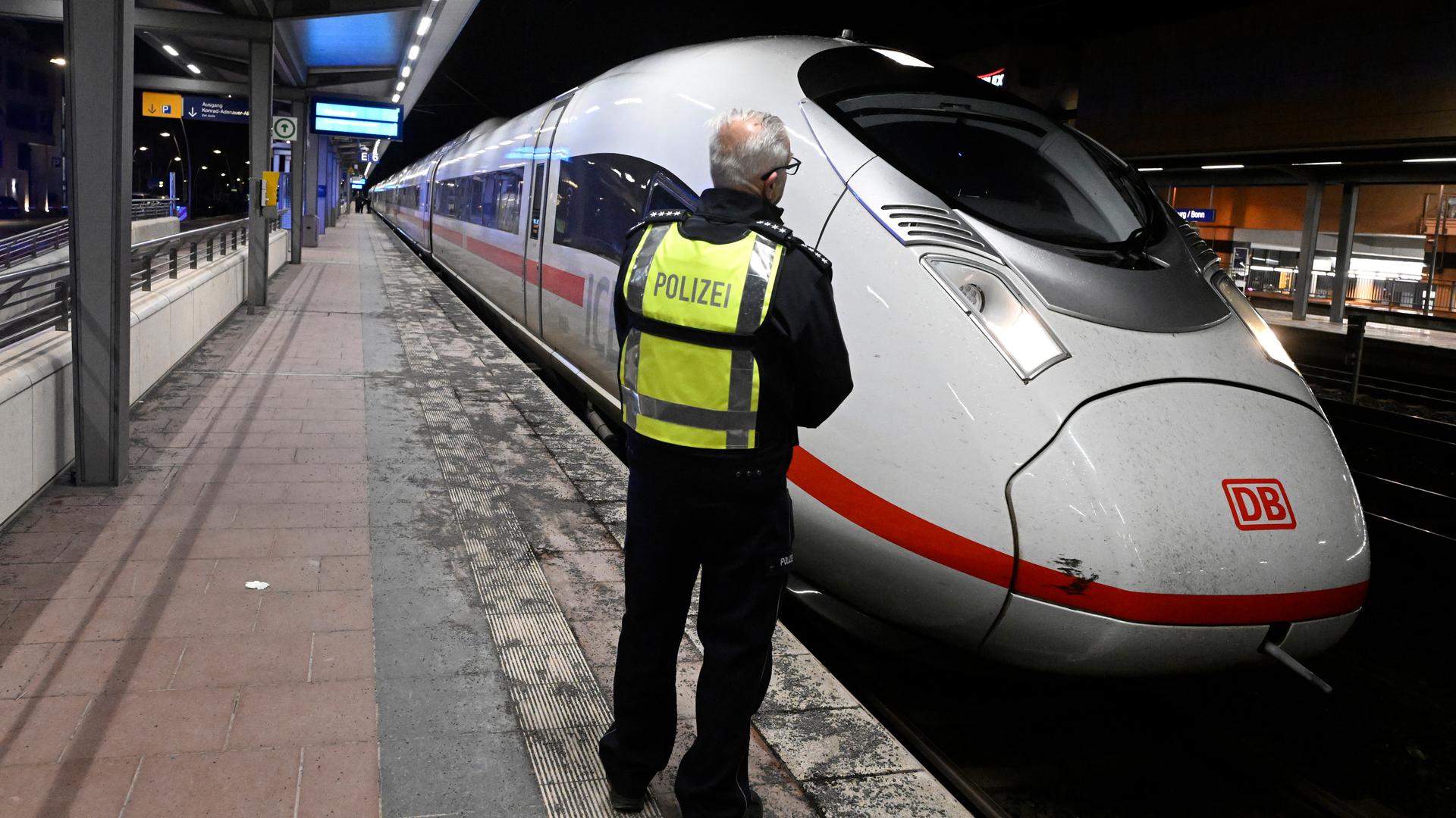 Ein Polizist steht auf einem Bahnsteig im Bahnhof Siegburg, auf dem ein ICE der Deutschen Bahn steht.