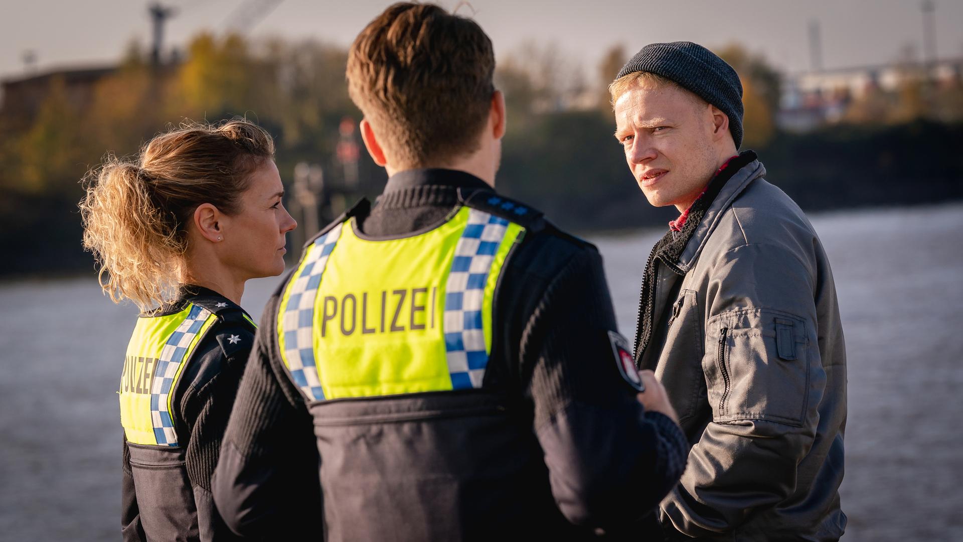 "Notruf Hafenkante - Nulllinie": Die Polizistin Franzi Jung (Rhea Harder-Vennewald) und ihr Kollege Nick Brandt (Raúl Richter) stehen nebeneinander vor Henner Schulte (Ilja Roßbander). Im Hintergrund ist die Elbe zu sehen.