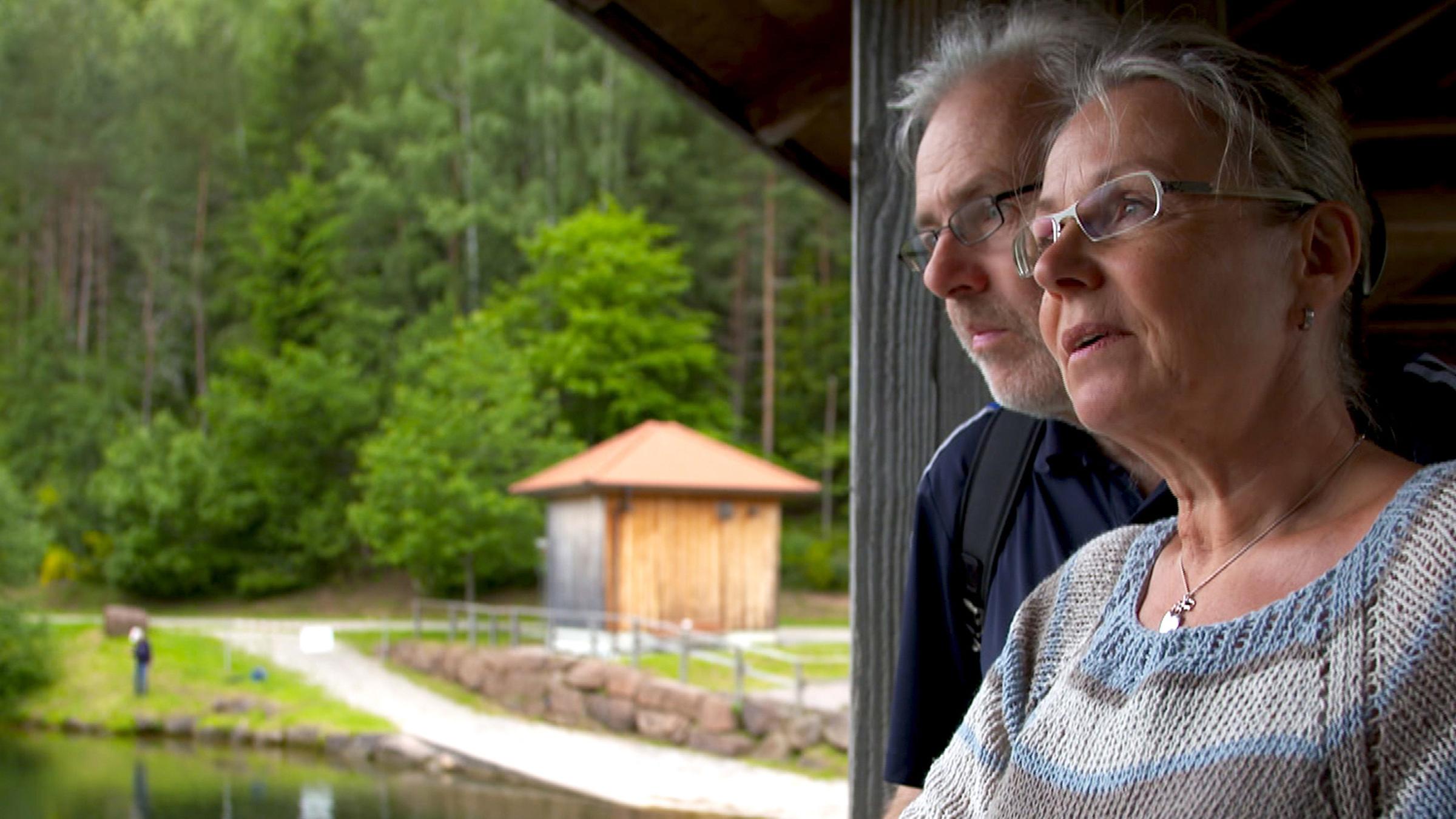 "37°: Nur das Heute zählt - Familienleben mit Demenz: Joachim hält Andrea im Arm. Sie stehen auf einer Holzbrücke, die über einen See führt, und schauen in die gleiche Richtung.