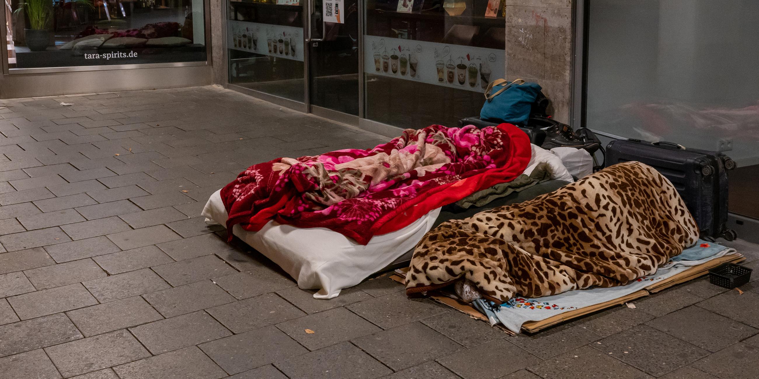Zwei Obdachlose schlafen in den frühen Morgenstunden in der Münchener Innenstadt vor der überdachten Fassade eine Ladenpassage.