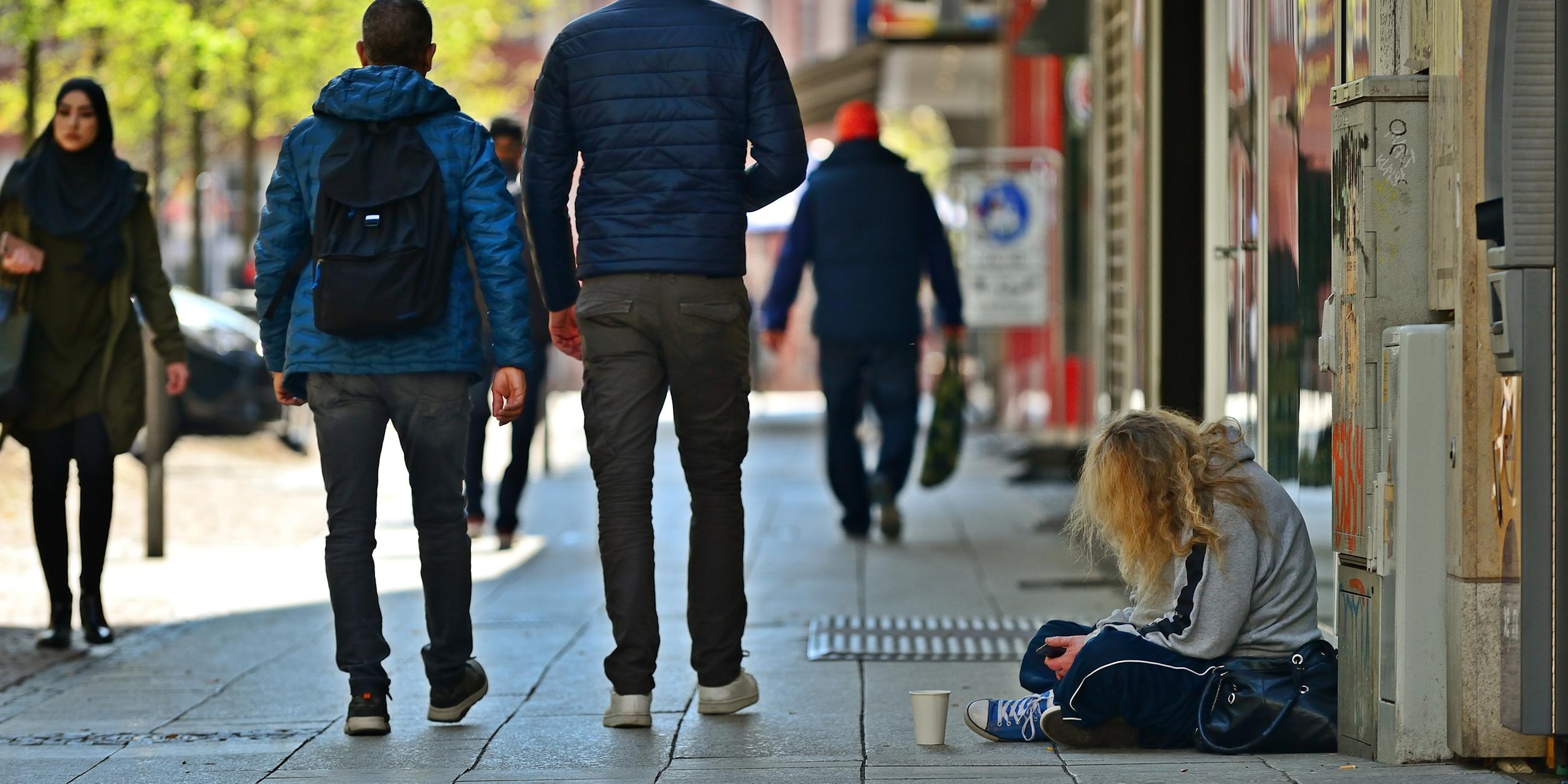 Obdachlose Frau in der Frankfurter Innenstadt, Passanten laufen an der Frau und ihrem Pappbecher in dem sie Spenden sammelt vorbei.