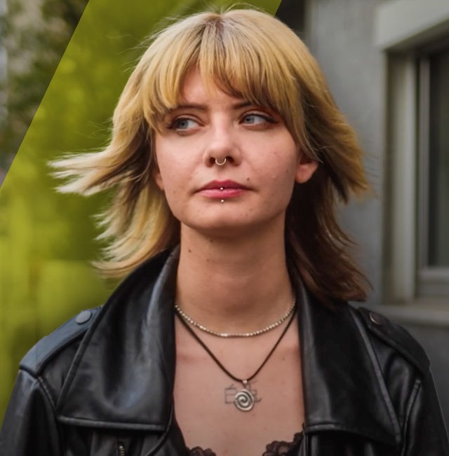 Eine junge Frau blickt nachdenklich zur Seite. Im Hintergrund ist eine Straße mit Häusern zu sehen.