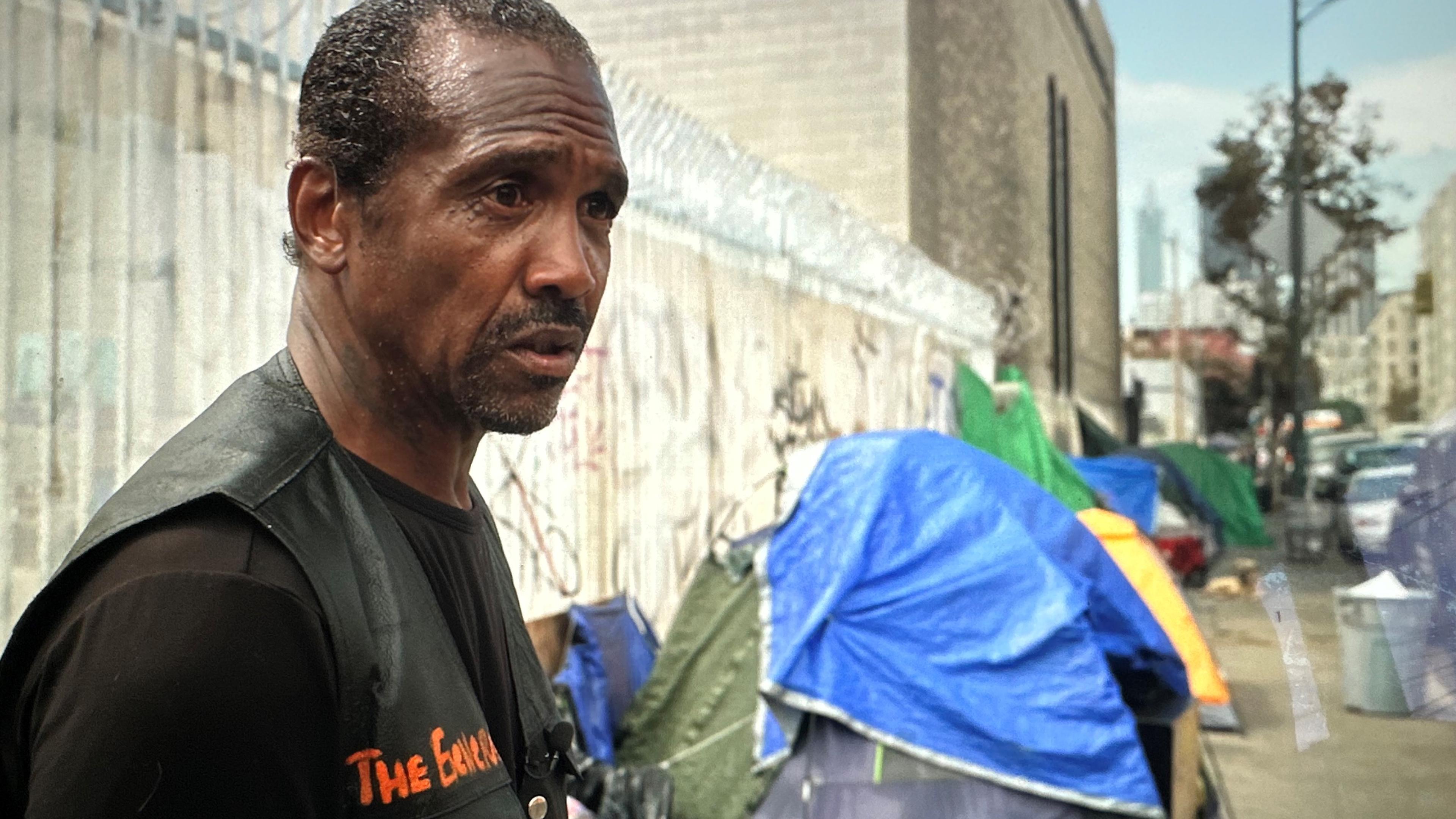 General Dogon, Obdachloser in LA, steht vor einigen Zelten, die am Wegrand stehen.