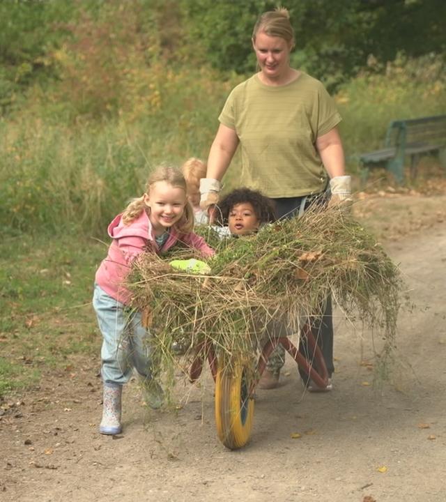 Eine Frau schiebt eine Schubkarre zusammen mit Kindern.