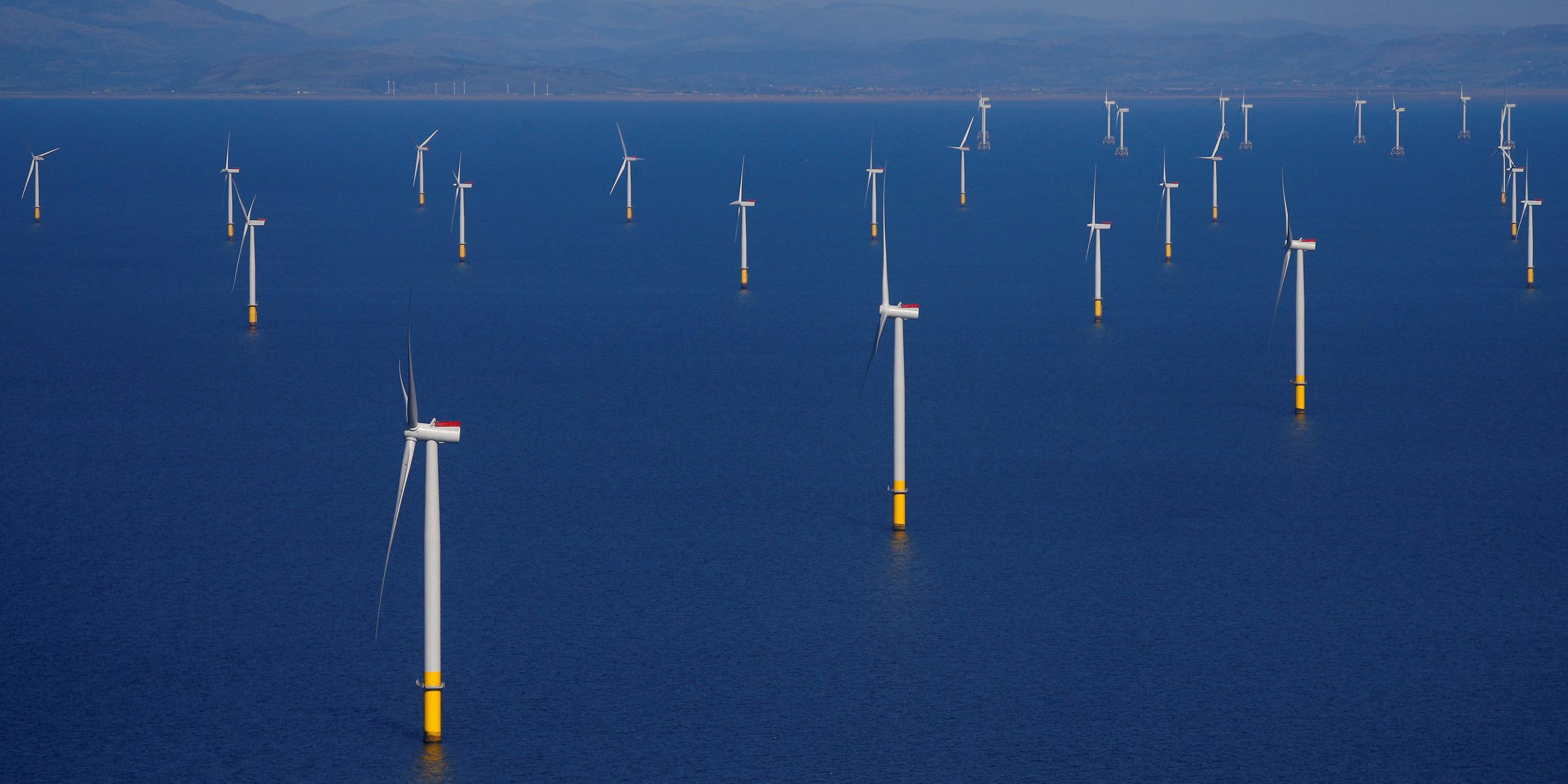 Mehrere Windräder zur Stromerzeugung stehen in Küstennähe im Meer.