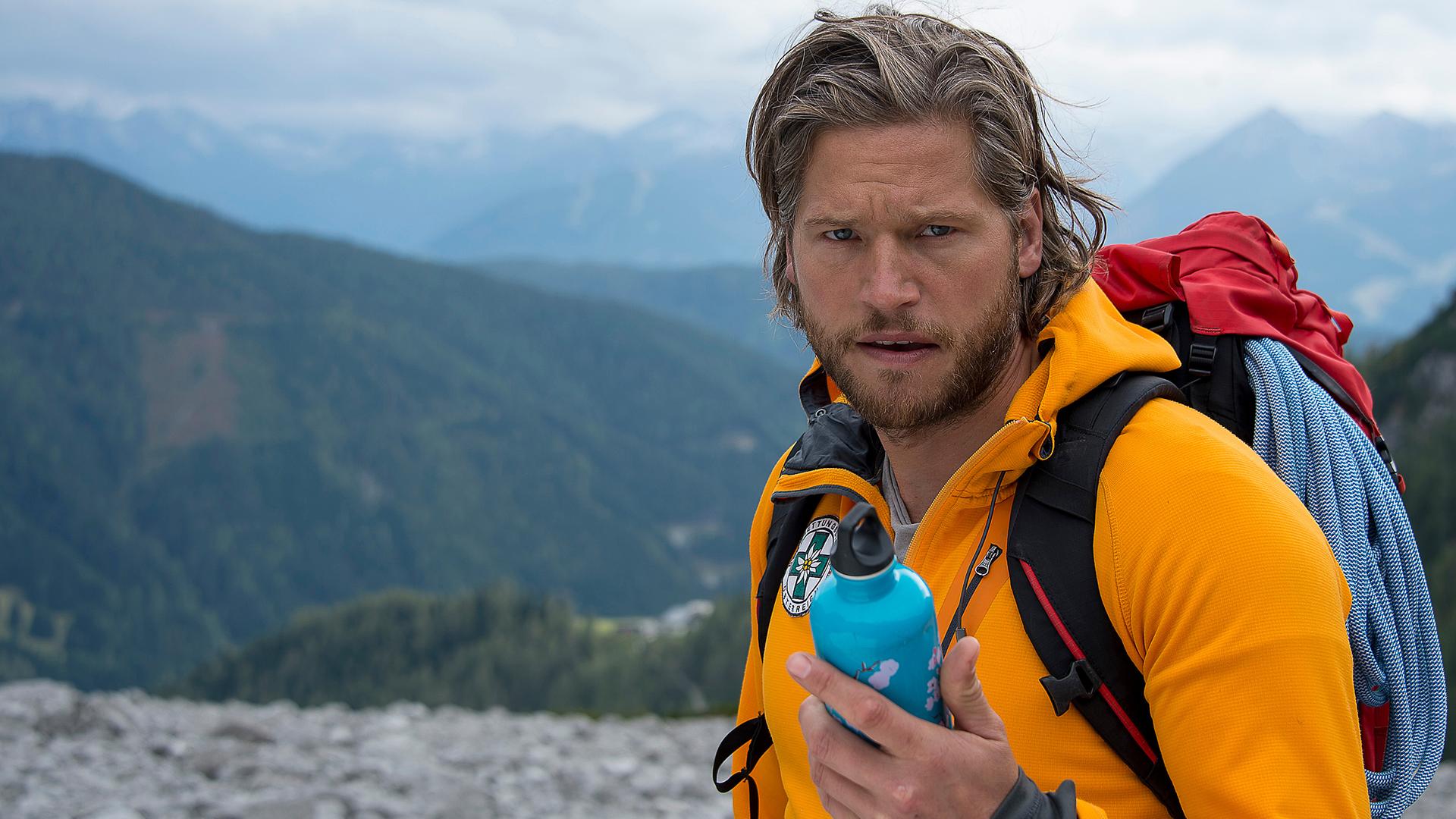 Markus (Sebastian Ströbel) steht in den Bergen und hält eine Isolierflasche in der Hand.