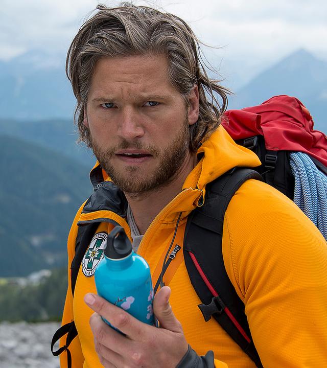 Markus (Sebastian Ströbel) steht in den Bergen und hält eine Isolierflasche in der Hand.